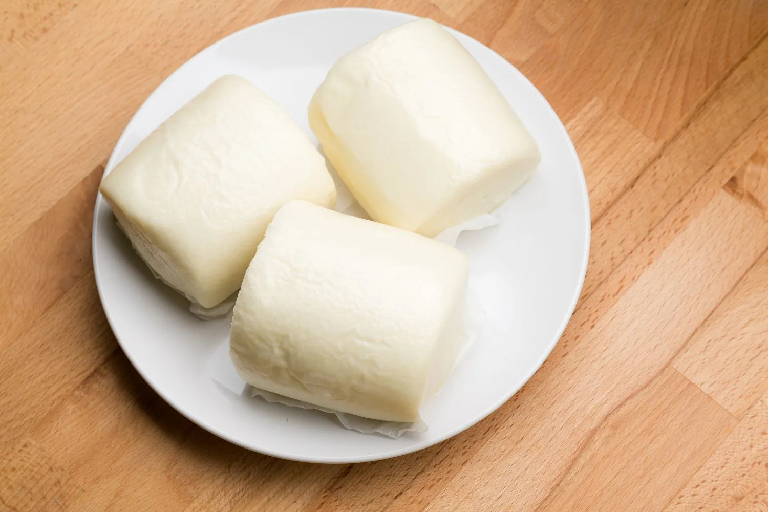 Three soft white steamed buns on a plate at Dragon Bay Bakery, a Chinese Bakery in Brooklyn